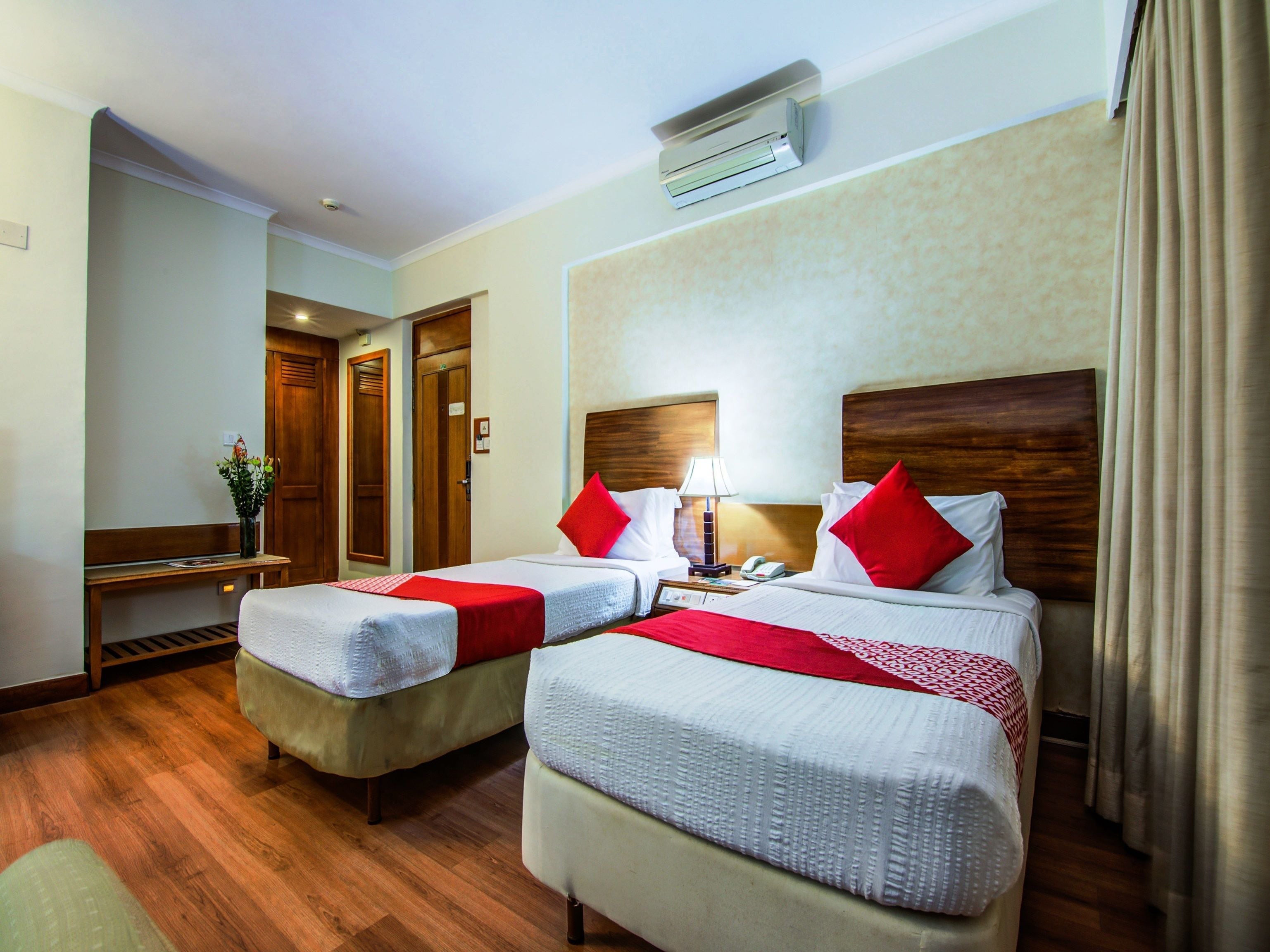 A hotel room with two beds, wooden flooring, a desk, and a nightstand.