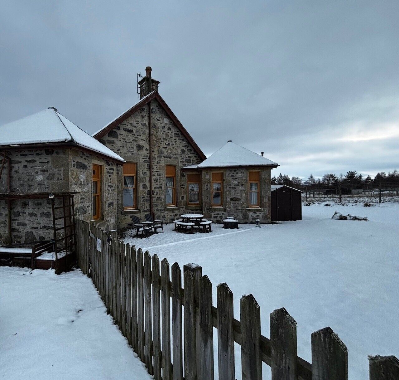 A stone building with a wooden fence, outdoor seating, and a snow-covered landscape.