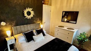 Quarto com cama, mesas de cabeceira, penteadeira, espelho e luminária no teto.