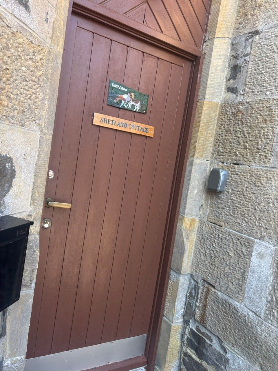 A wooden door with a sign reading "Shetland Cottage" and a small plaque with a horse illustration.