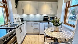 Uma cozinha moderna com armários brancos, um fogão de aço inoxidável e uma área de jantar com mesa e cadeiras.