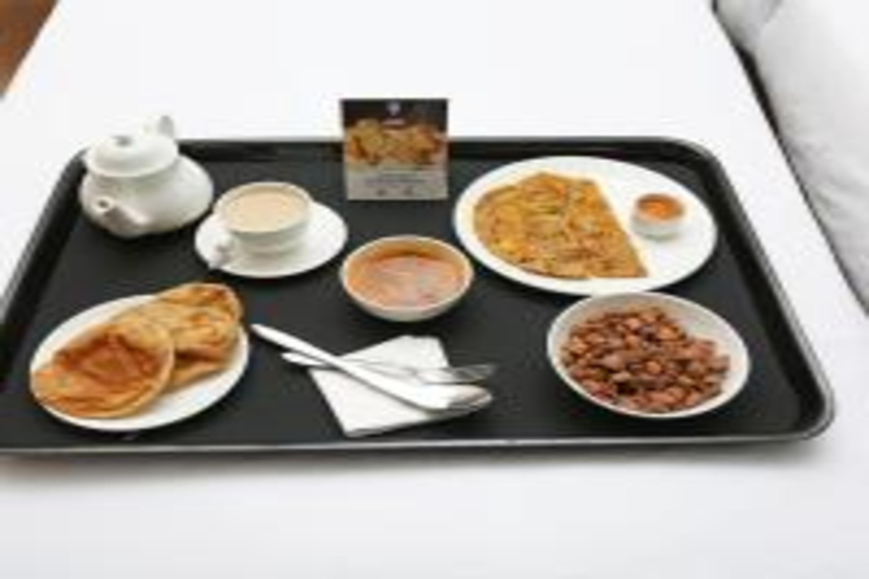 Una bandeja con un juego de té, tazas, un plato de comida, un tazón de sopa y una bandeja de galletas.