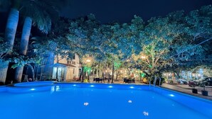 Piscina al aire libre de noche con árboles circundantes e iluminación ambiental.