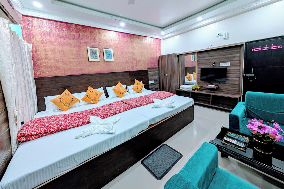 A modern hotel room with a large bed, a TV, a wardrobe, and a seating area with a table and chairs.