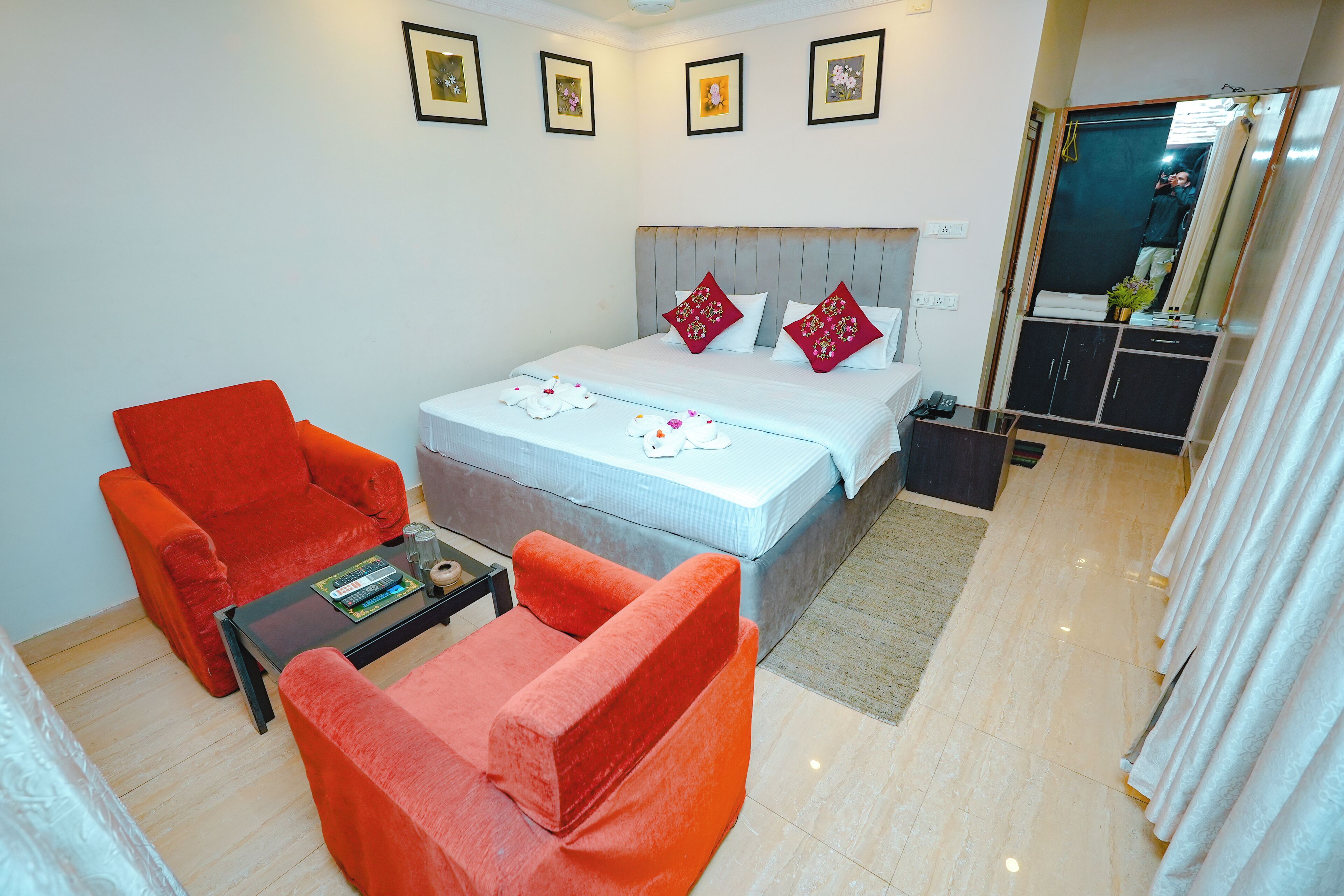 Quarto de hotel com uma cama, duas cadeiras vermelhas, uma mesa pequena e um espelho.