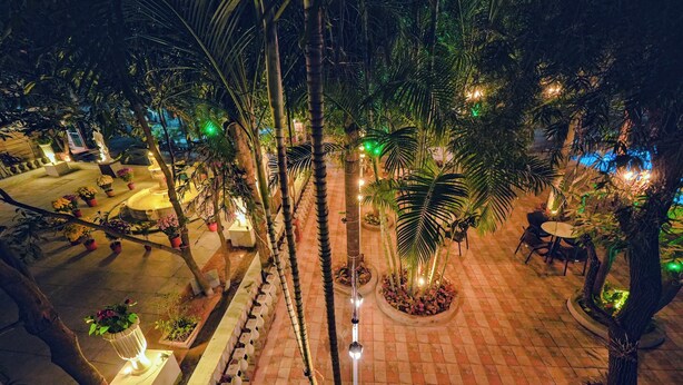 Un espacio exterior bien iluminado con plantas en macetas, una fuente y arreglos de asientos.