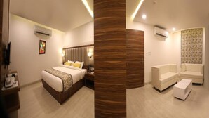A modern hotel room with a bed, a seating area with a sofa and armchairs, a wooden accent wall, and a patterned wallpaper on the wall. - Hotel Narayanam (Kota)