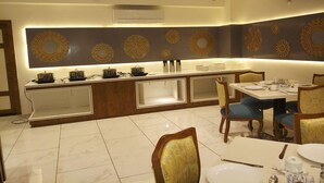 A modern kitchen with a central island, a dining area with blue chairs, and decorative wall art. - Hotel Narayanam (Kota)