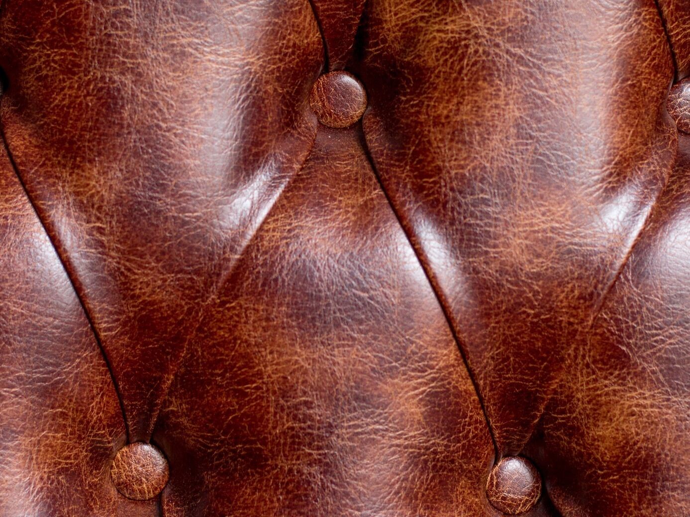 A close-up of a brown leather surface with a tufted design and round buttons.