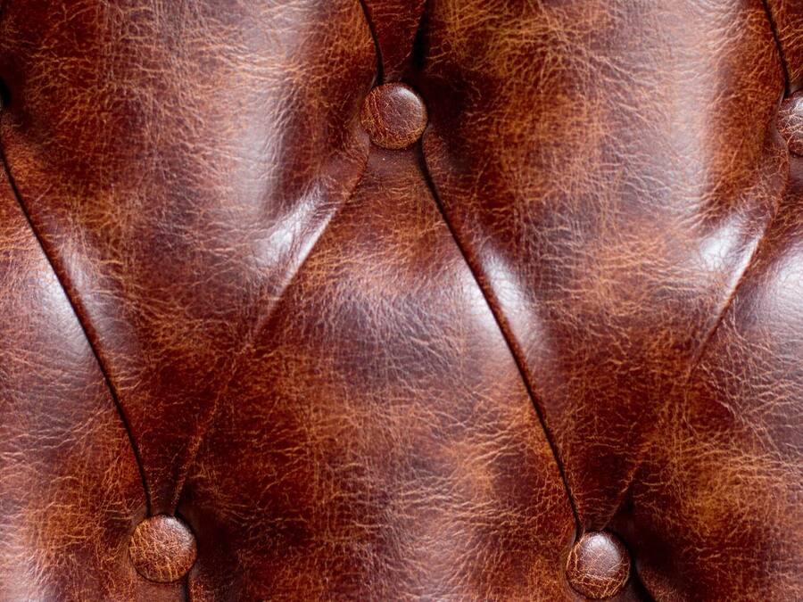 Een detailopname van een bruin lederen oppervlak met een gesneden patroon en ronde knopen.