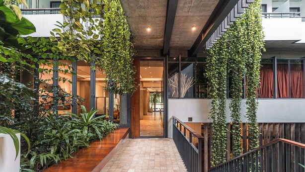 A modern indoor space with a wooden floor, a staircase with a black railing, and hanging greenery. - Penh House Hotel (Phnom Penh)