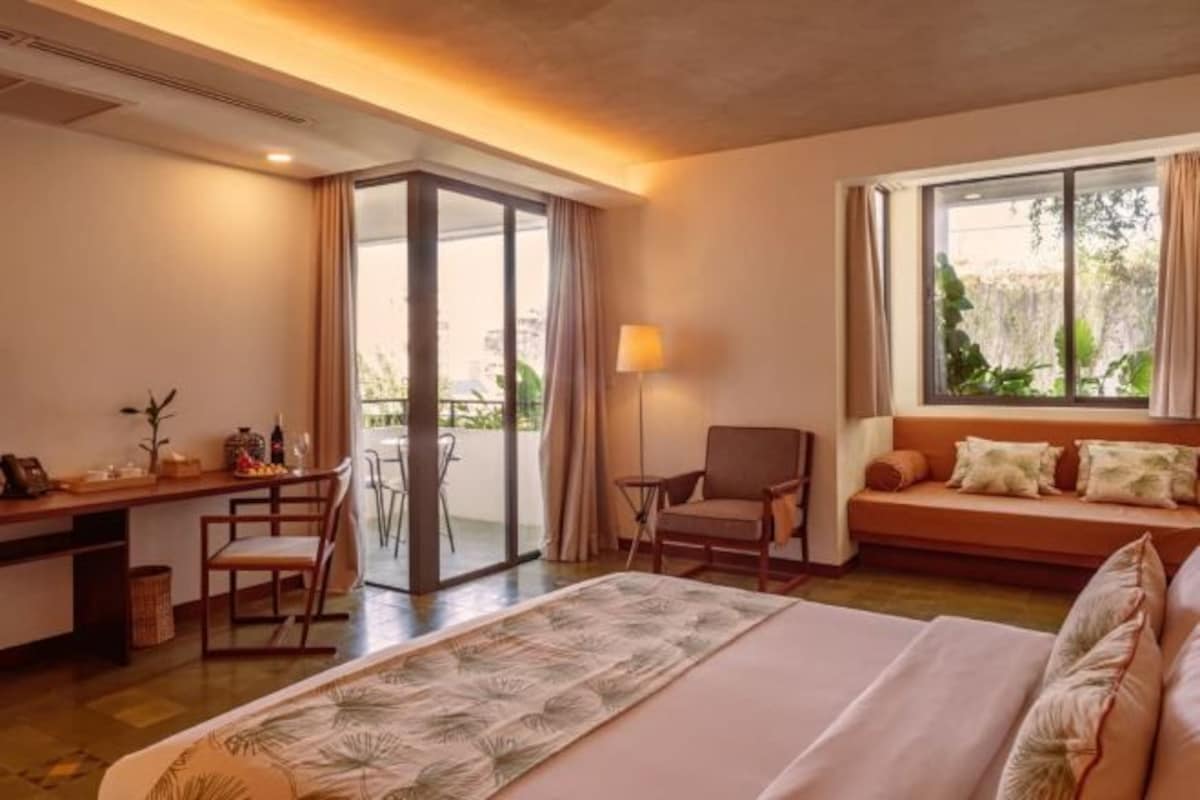 Una habitación de hotel con cama, escritorio con silla, sofá y ventana con cortinas.