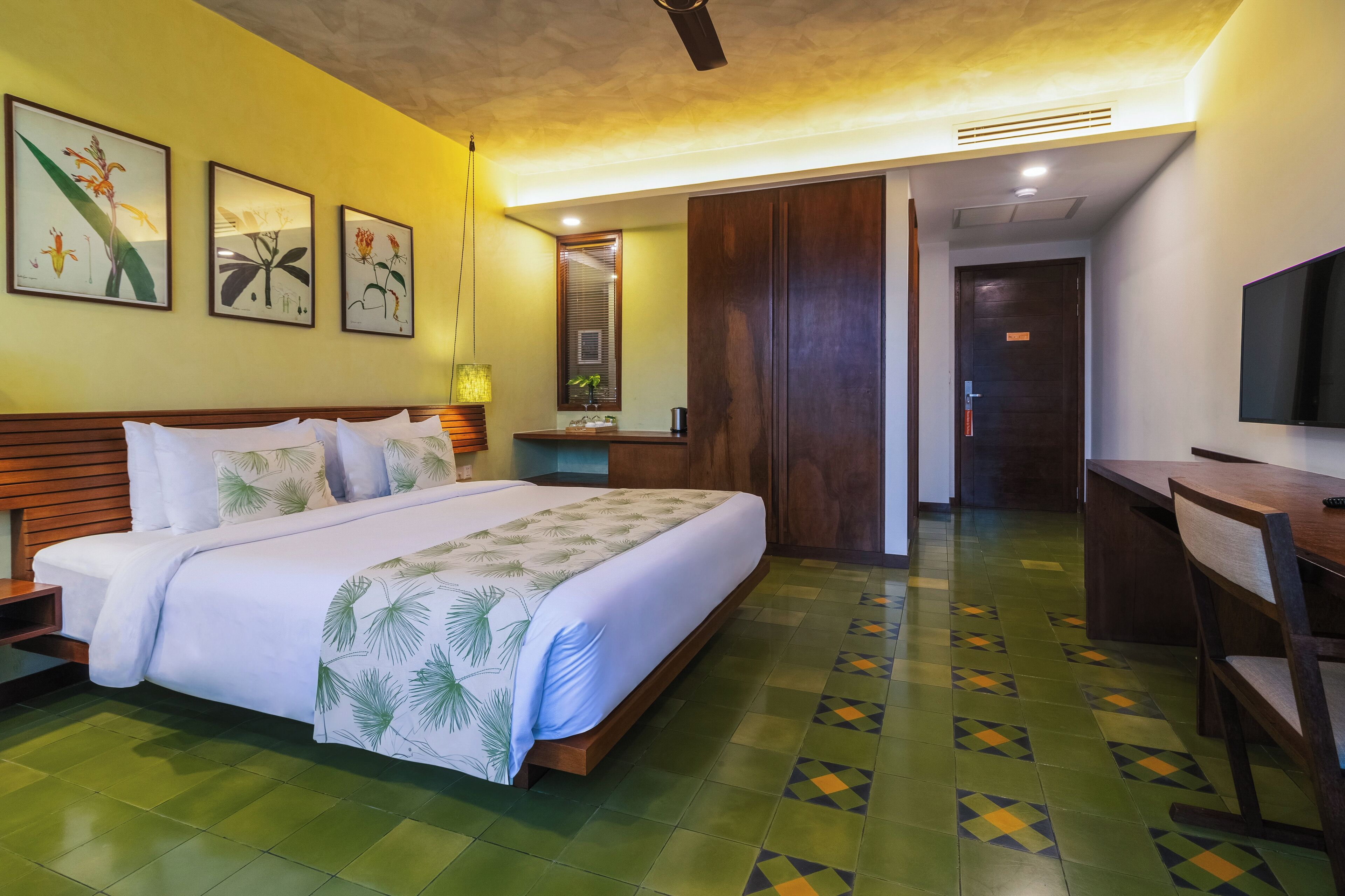 A hotel room with a large bed, a desk, a television, and artwork on the wall.