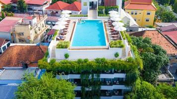 Una piscina en la azotea con sillones de descanso y sombrillas, rodeada de vegetación y arquitectura tradicional.