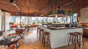 A modern bar area with a city view, wooden ceiling, and bar stools. - Penh House Hotel (Phnom Penh)