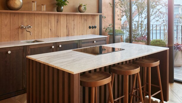 A modern kitchen with a central island, wooden flooring, and large windows offering a view of the outdoors. - The Emerald (Prague)