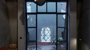 A modern interior with a large black sculpture, a wooden bench, a round table, and a large window with a view of the outside. - The Emerald (Prague)