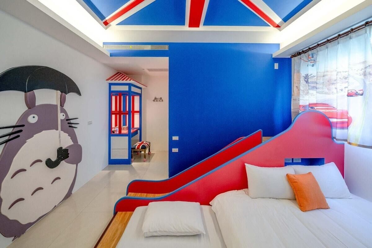A bedroom with a bed, pillows, a red and blue wall, and a large cartoon character mural.