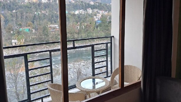 Uma varanda com vista para um rio e montanhas. Há uma mesa e duas cadeiras.