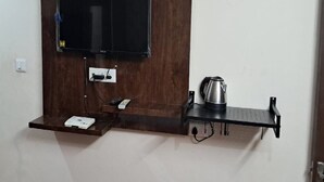 Televisão fixada na parede, com uma régua de tomadas e uma chaleira num prateleira.