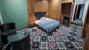 Quarto com cama, mesa de cabeceira, cadeira, guarda-roupa e tapete estampado.