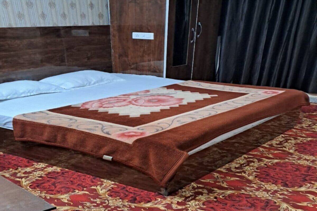 A bed with a floral bedspread, a red patterned rug, and a wooden headboard.