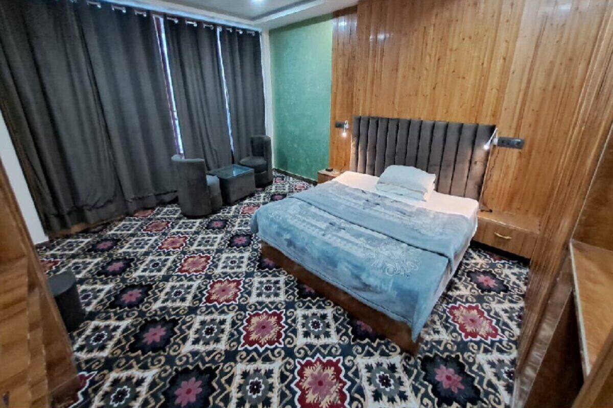 A bedroom with a patterned carpet, a bed with a headboard, a nightstand, a chair, and a wardrobe.