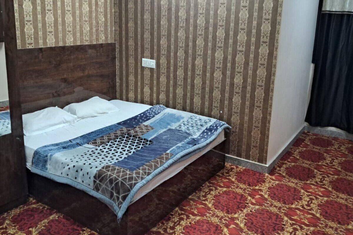 A neatly made bed with a patterned bedspread, a wooden headboard, and a red patterned carpet.