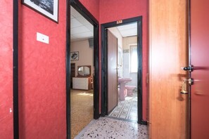A hallway with a red wall and a wooden door leading to a bathroom with a pink toilet and sink. - Albergo Ristorante Stella (Palestrina)