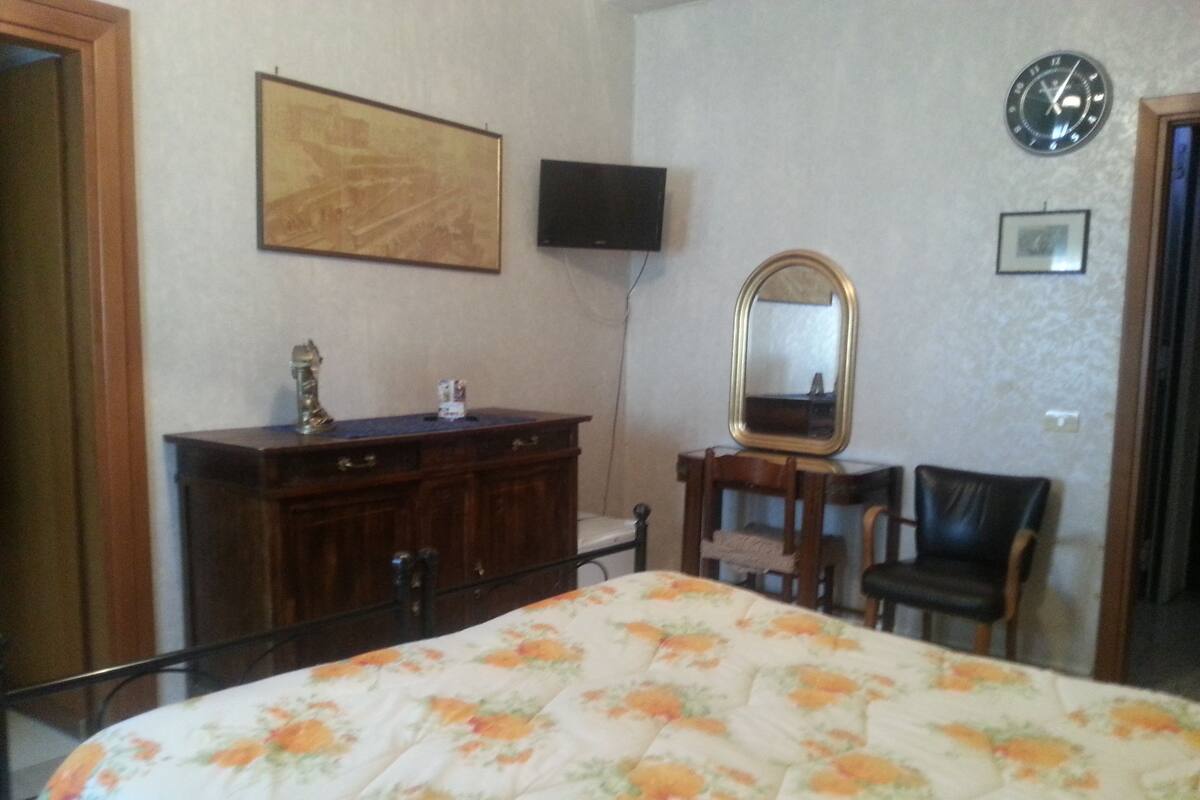 A bedroom with a bed, a dresser, a mirror, a clock, and a television on the wall.