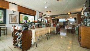 A spacious dining area with a long table covered by a tablecloth, surrounded by wooden cabinets and shelves with various items. - Albergo Ristorante Stella (Palestrina)