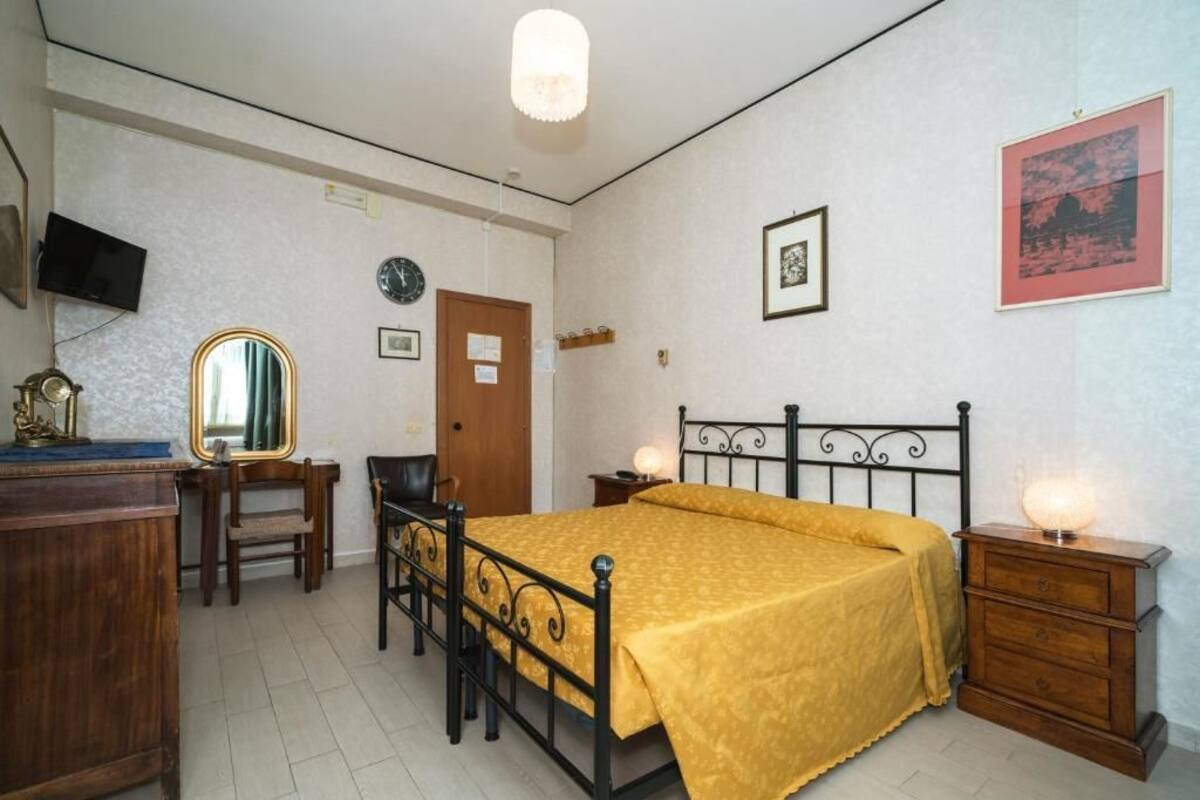 A bedroom with a bed, wooden dresser, desk, chair, and a television on the wall.