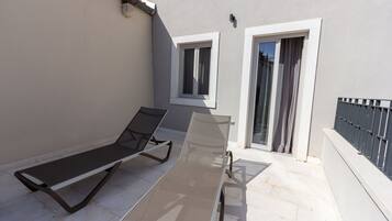Un balcon avec deux chaises longues, une petite fenêtre et une porte-fenêtre coulissante.