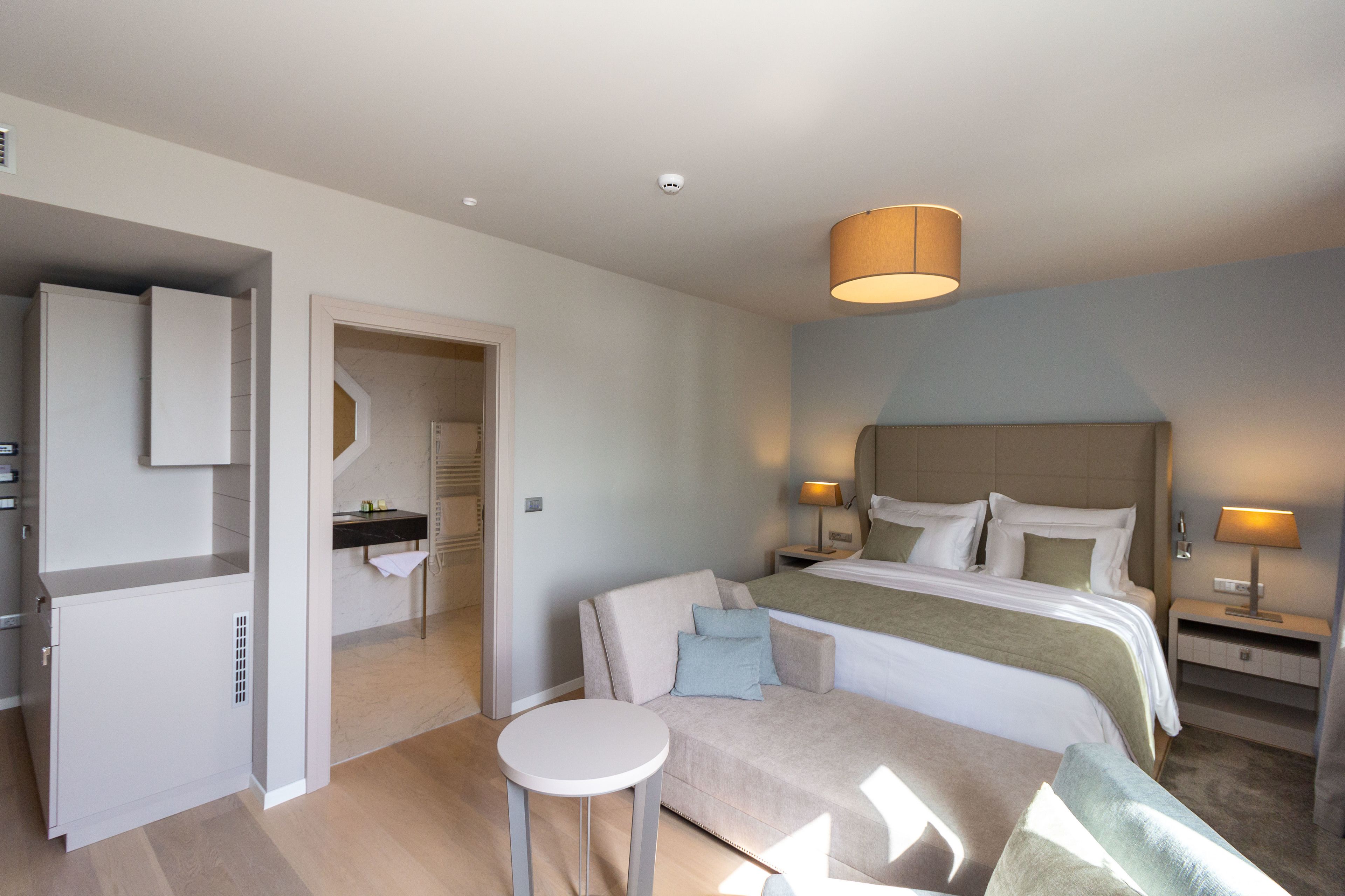 Ett modernt hotellrum med en säng, en soffa, ett litet bord och ett badrum med spegel och handduksställ.