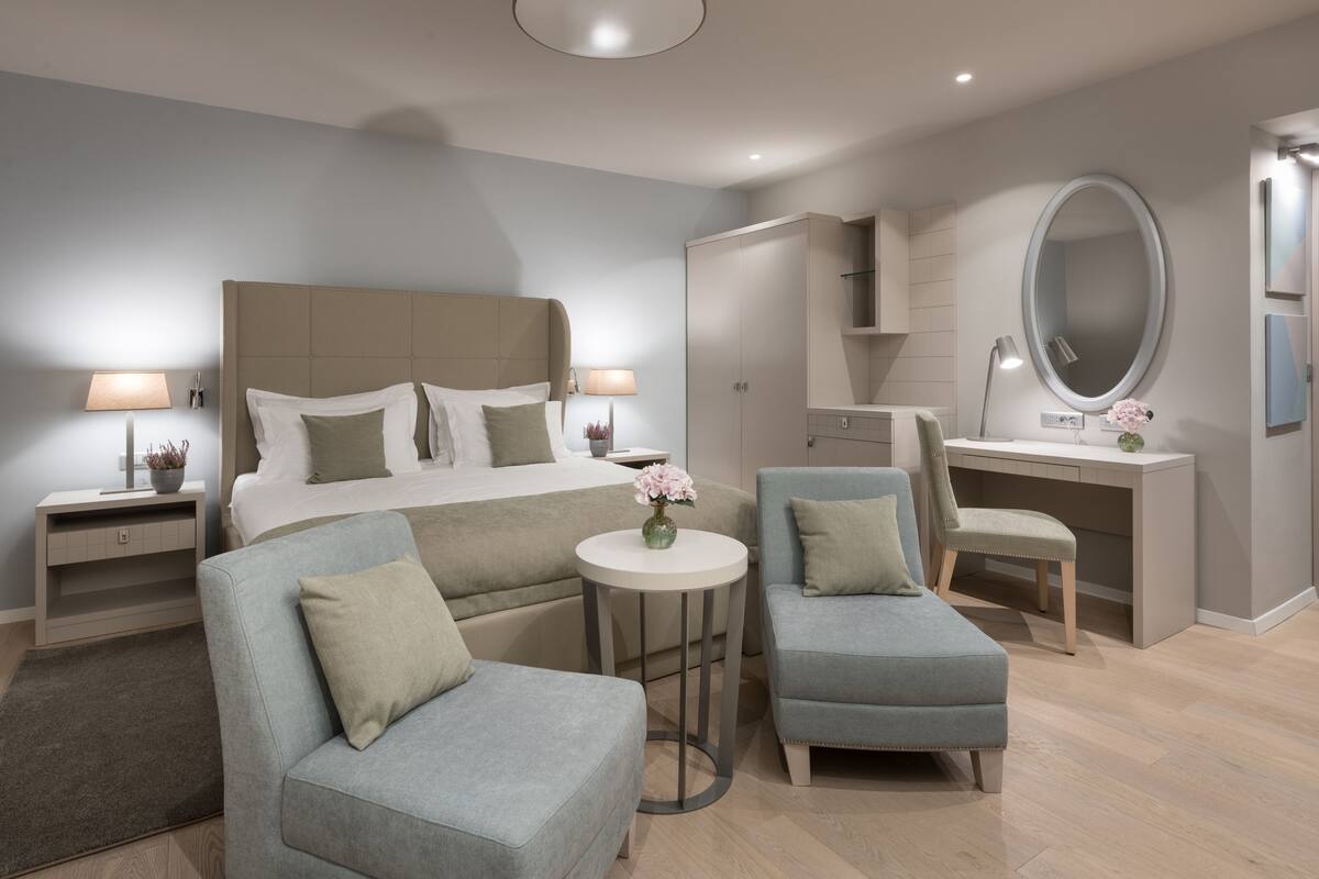 Un dormitorio moderno con una cama grande, dos sillones, un escritorio y un espejo redondo.