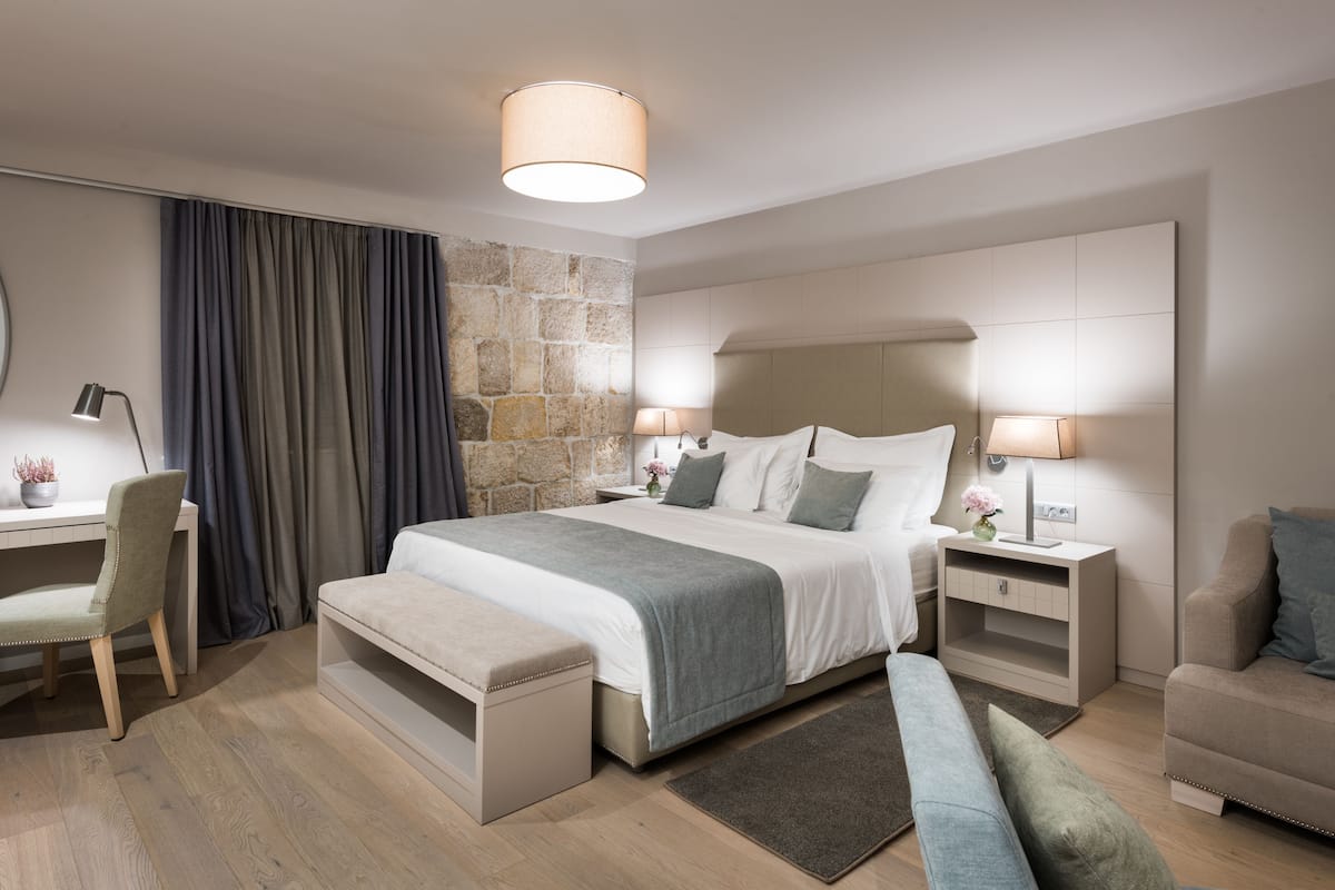 Una habitación de hotel moderna con una cama grande, mesitas de noche con lámparas, un escritorio con una silla y un banco.
