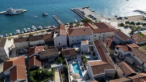 Un pueblo costero con edificios de tejas rojizas, un puerto deportivo con barcos y una piscina.