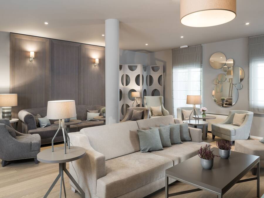 Una sala de estar moderna con un sofá beige grande, dos sillones, una mesa de centro y una mesita auxiliar con una lámpara. Se observan paneles decorativos en la pared y un espejo con diseños circulares.