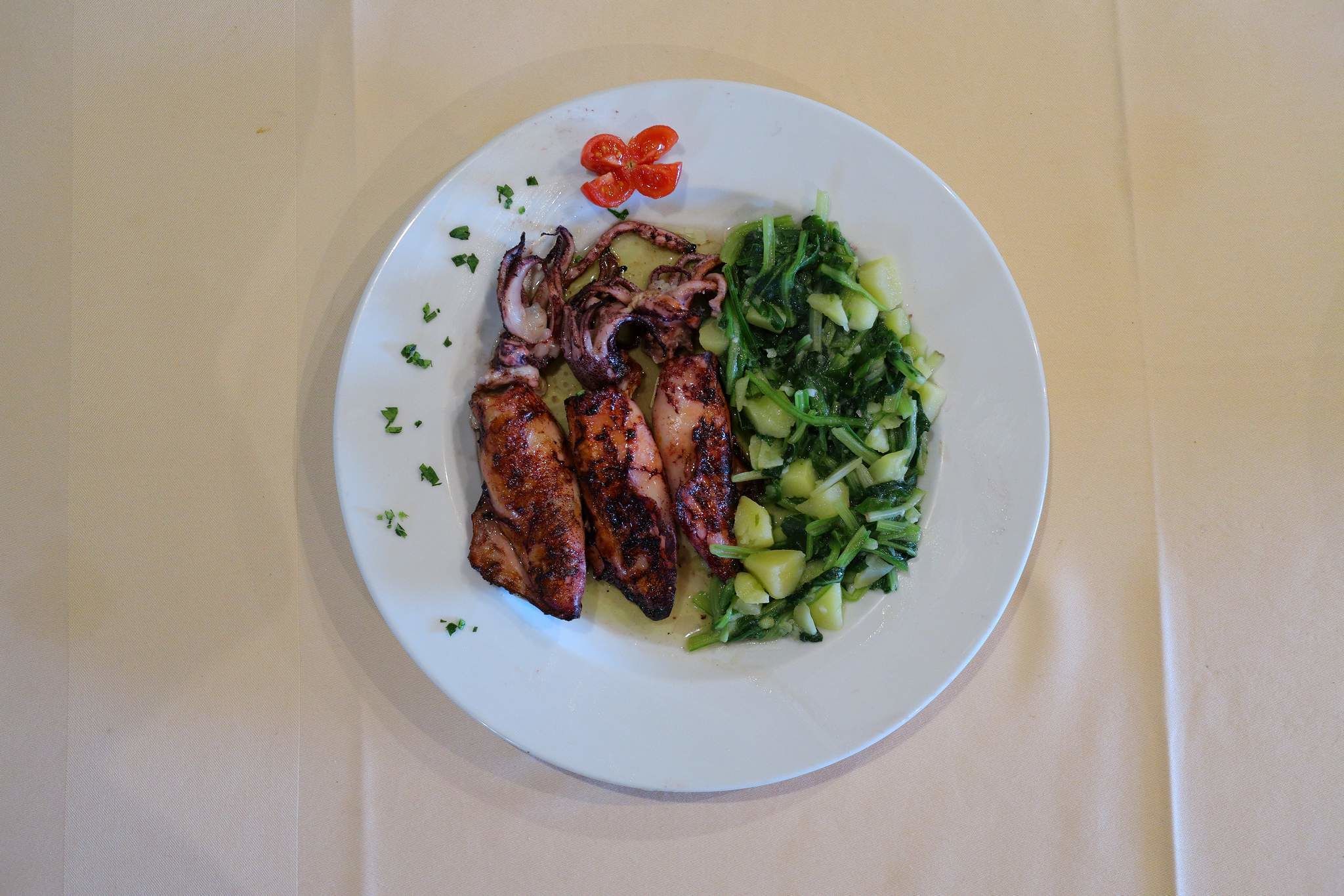 A plate with grilled chicken, a side of greens, and a cherry tomato.