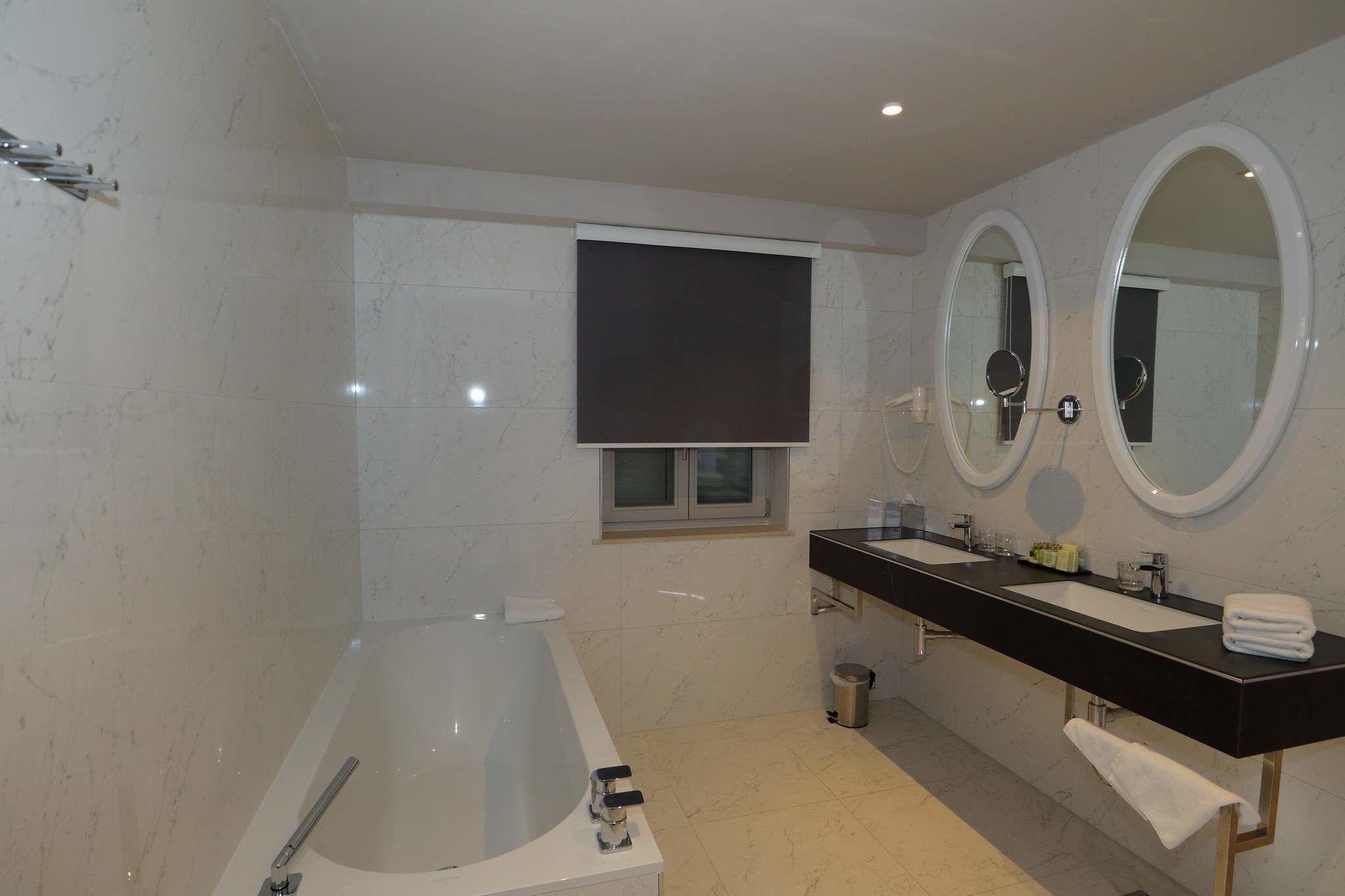 Een moderne badkamer met een badkuip, twee wastafels en drie spiegels.