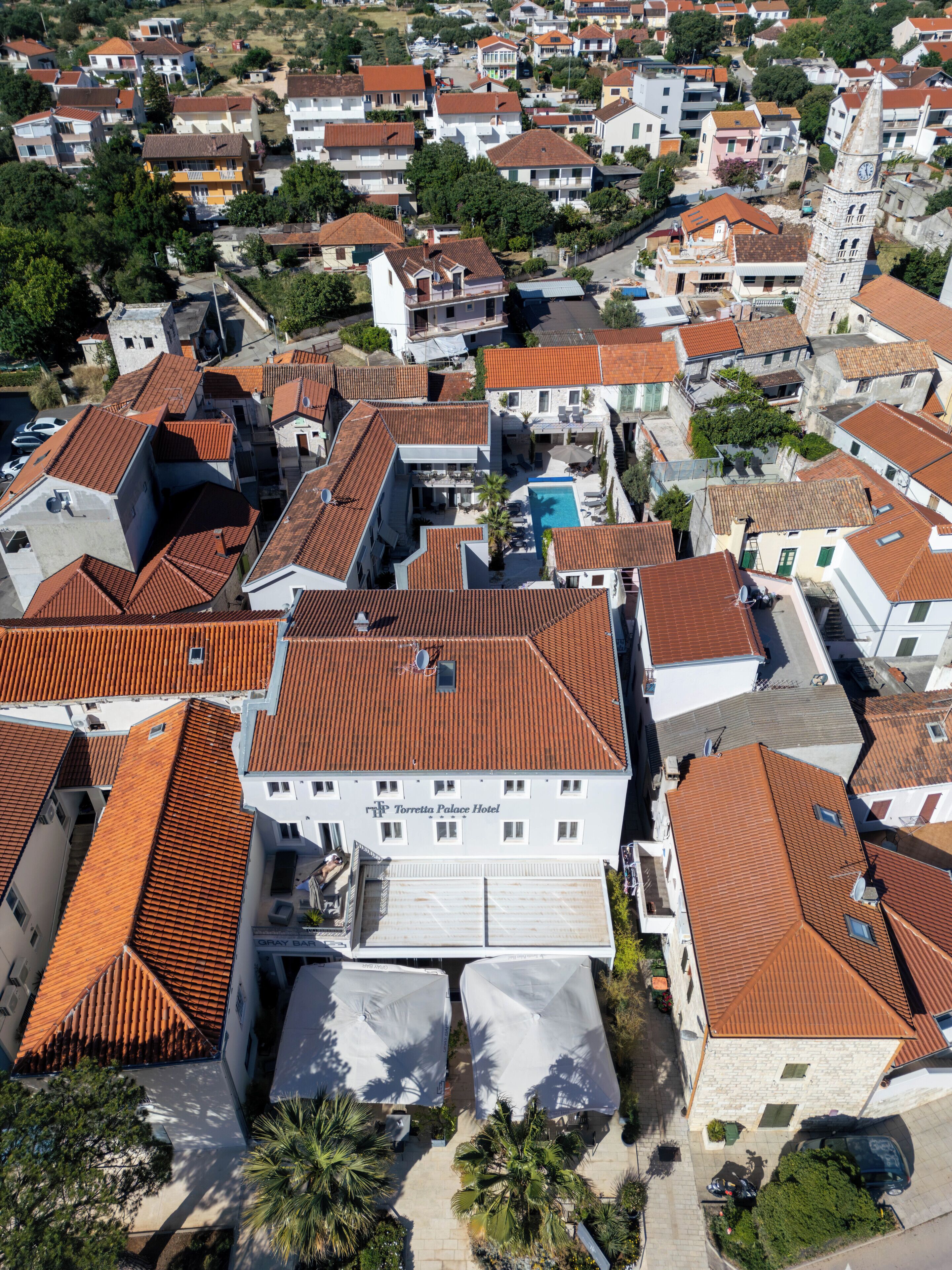 An aerial view of a residential area with a prominent hotel featuring a swimming pool and a clock tower.