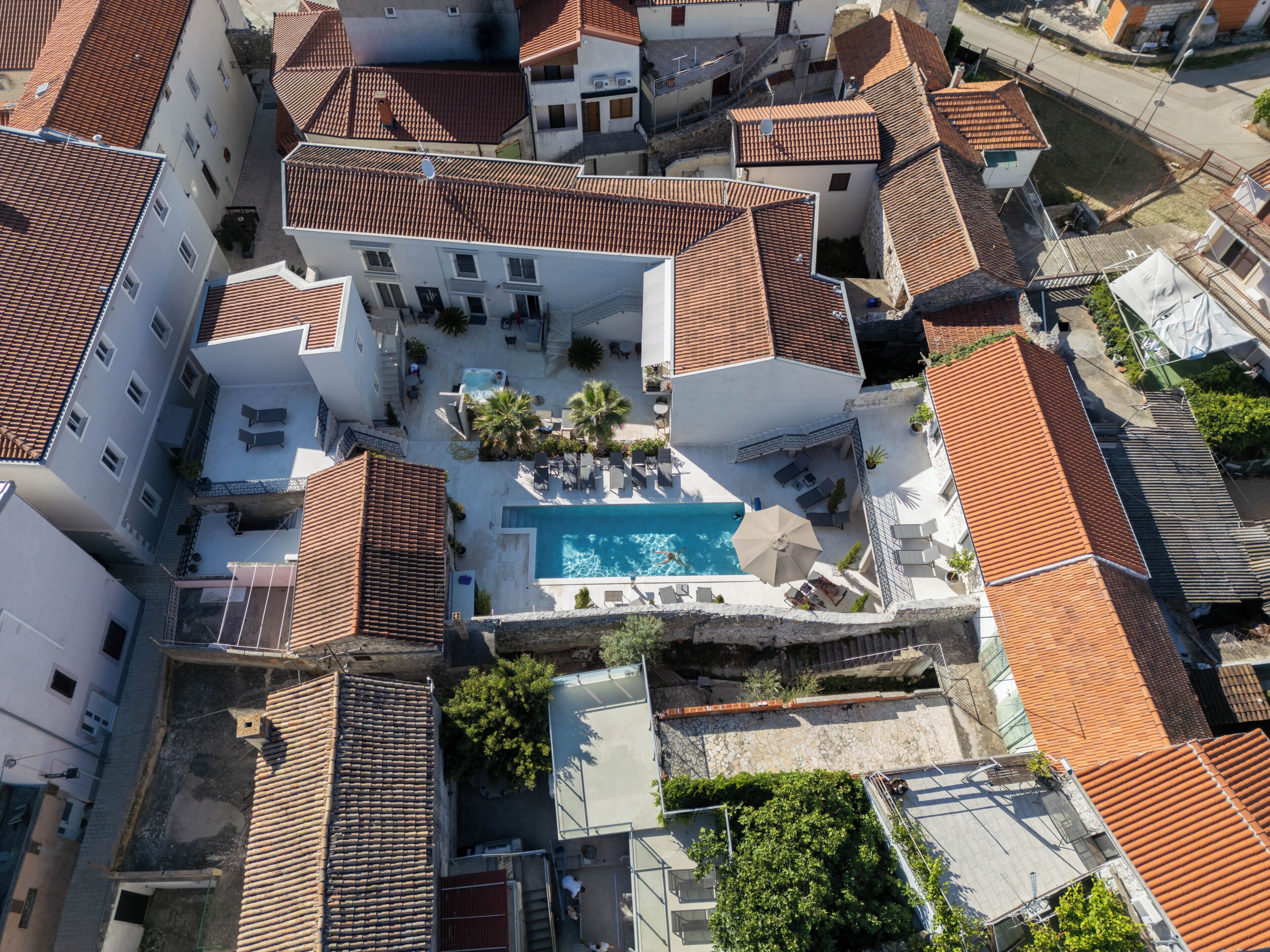 An aerial view of a residential area with a swimming pool surrounded by buildings with red-tiled roofs.