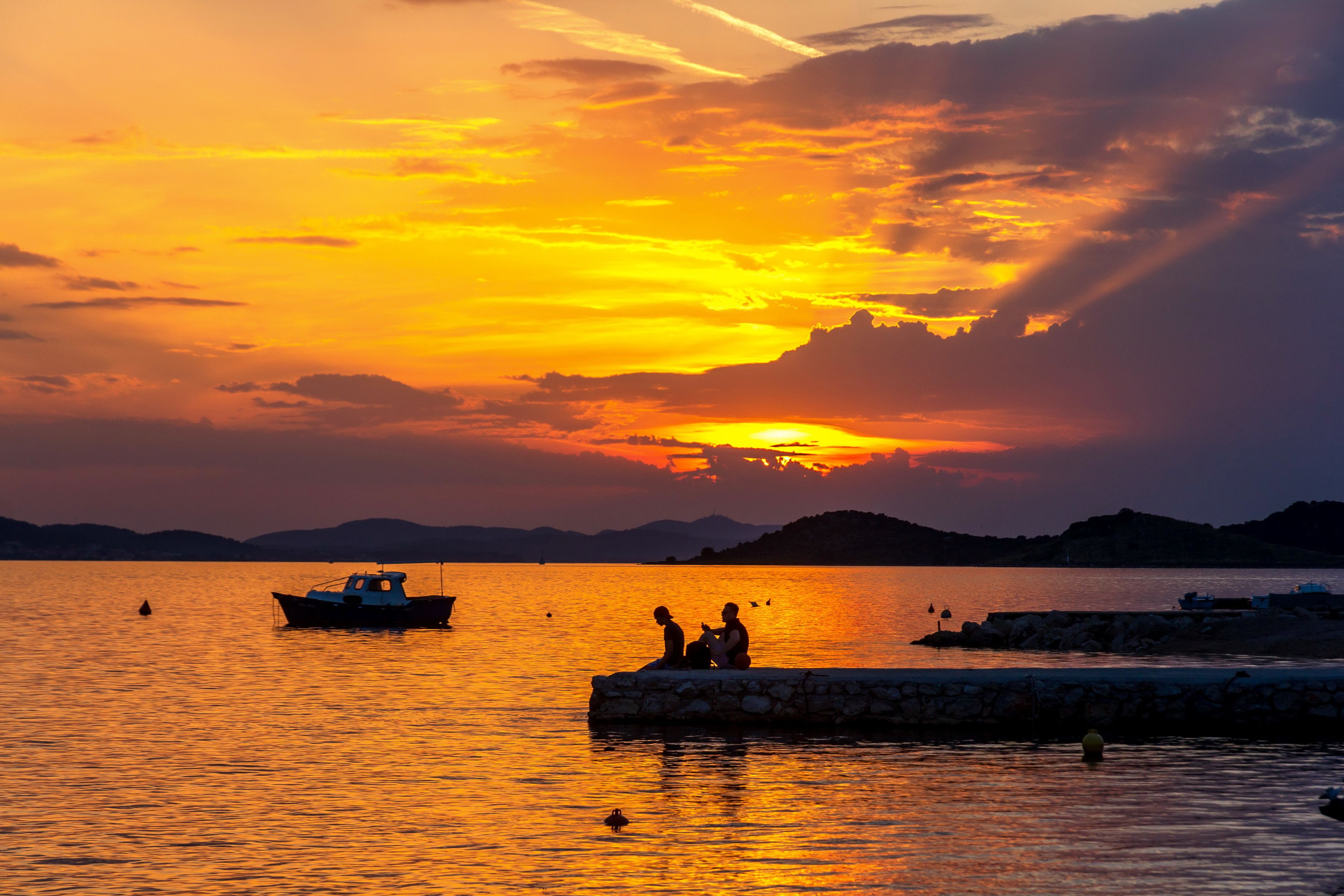 A sunset over a calm body of water with boats and a stone pier.