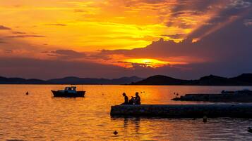 A sunset over a calm body of water with boats and a stone pier.