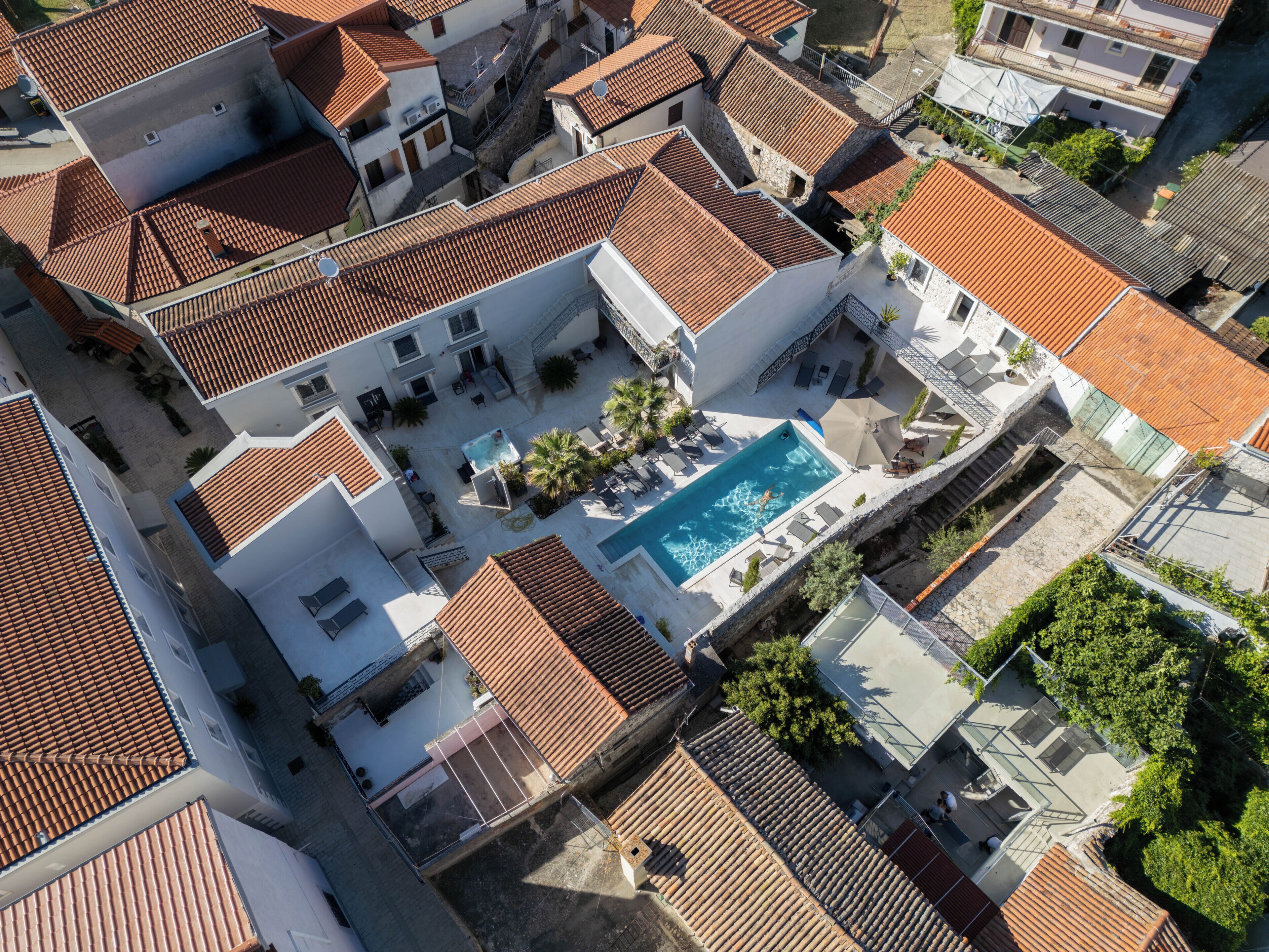 Vista aérea de um bairro residencial com telhados de terracota, piscina e vegetação ao redor.
