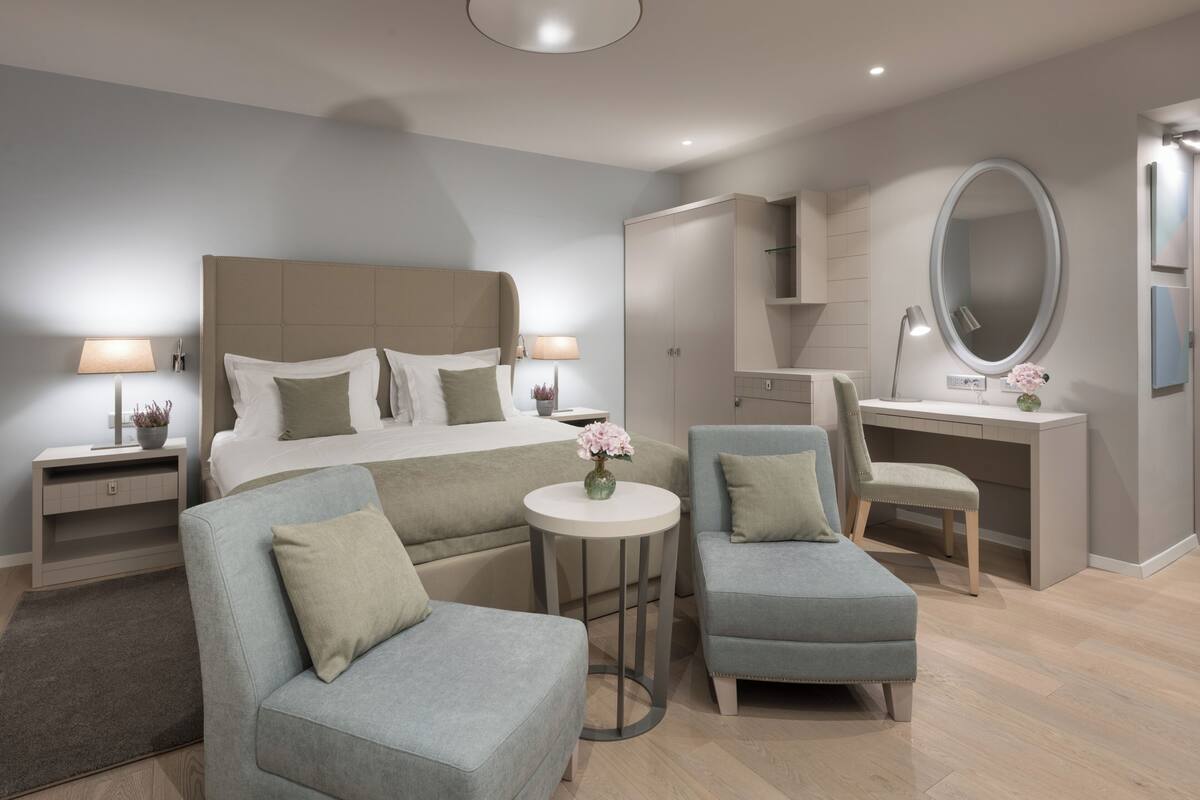 Un dormitorio moderno con una cama grande, dos sillones, un escritorio y un espejo redondo.