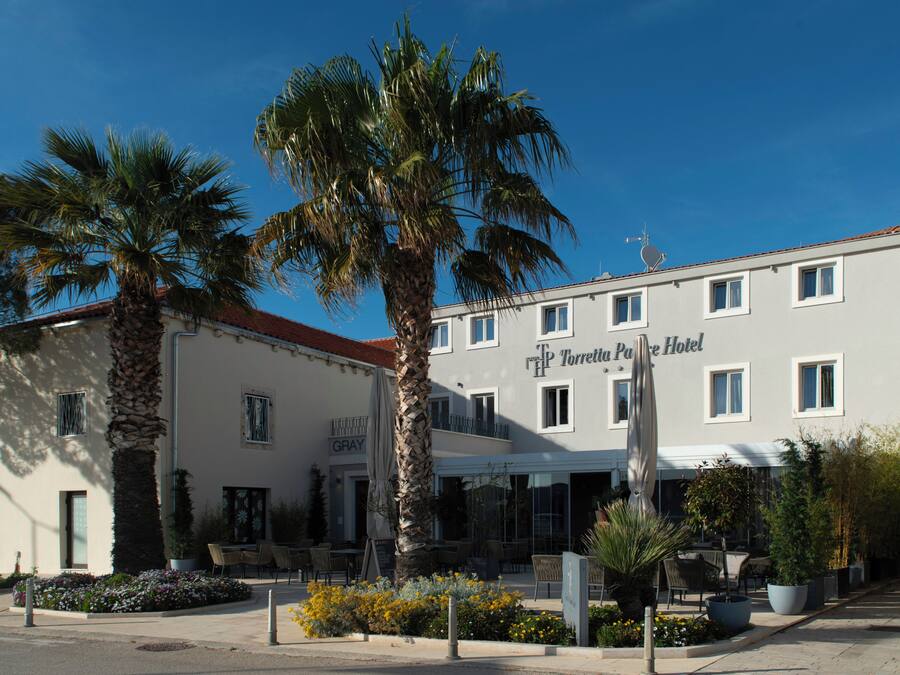 Ein Hotel mit Terrasse, Palmen und Außenbestuhlung.