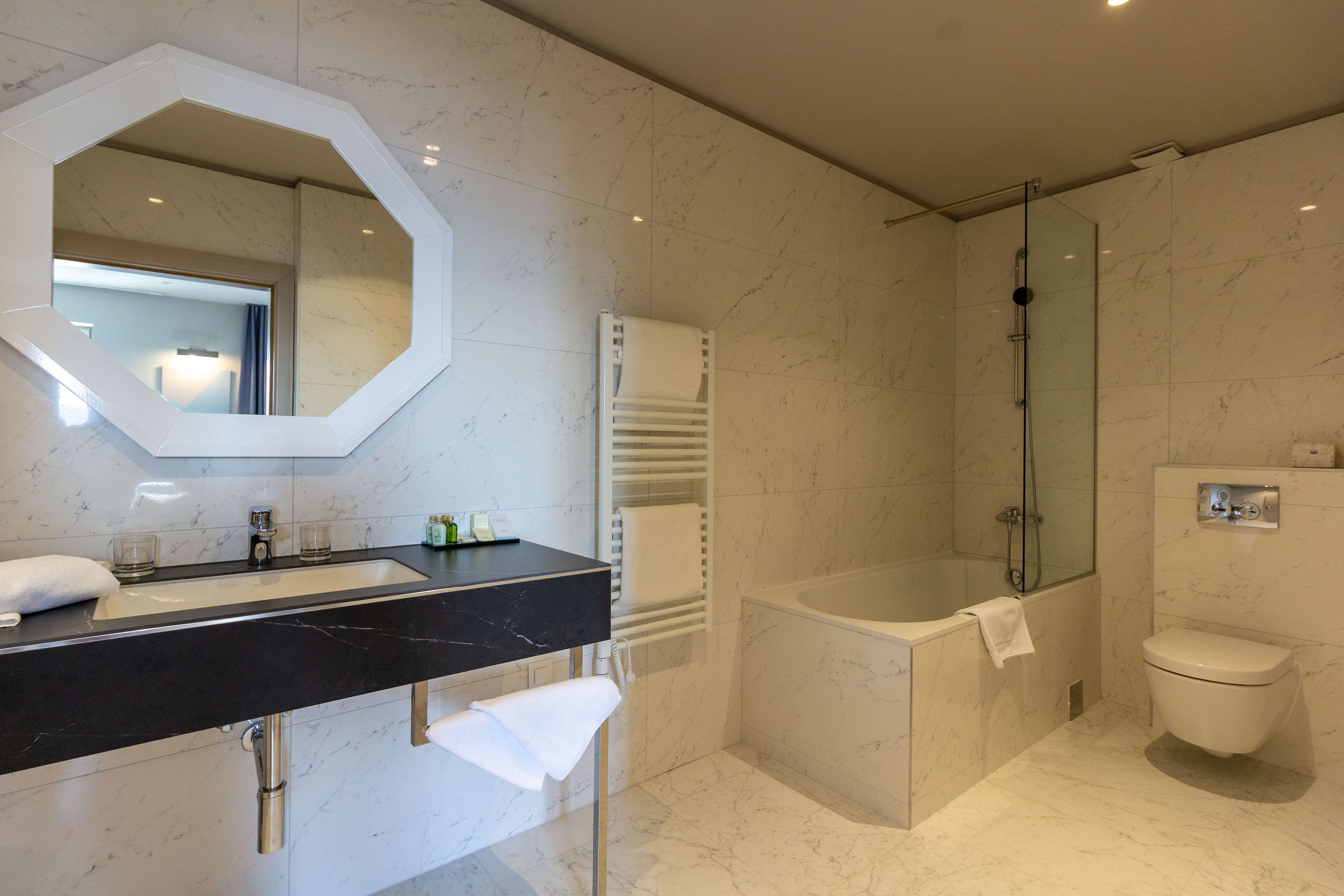 Un baño moderno con un lavabo de mármol negro, un espejo grande, ducha envuelta en vidrio y un inodoro blanco.