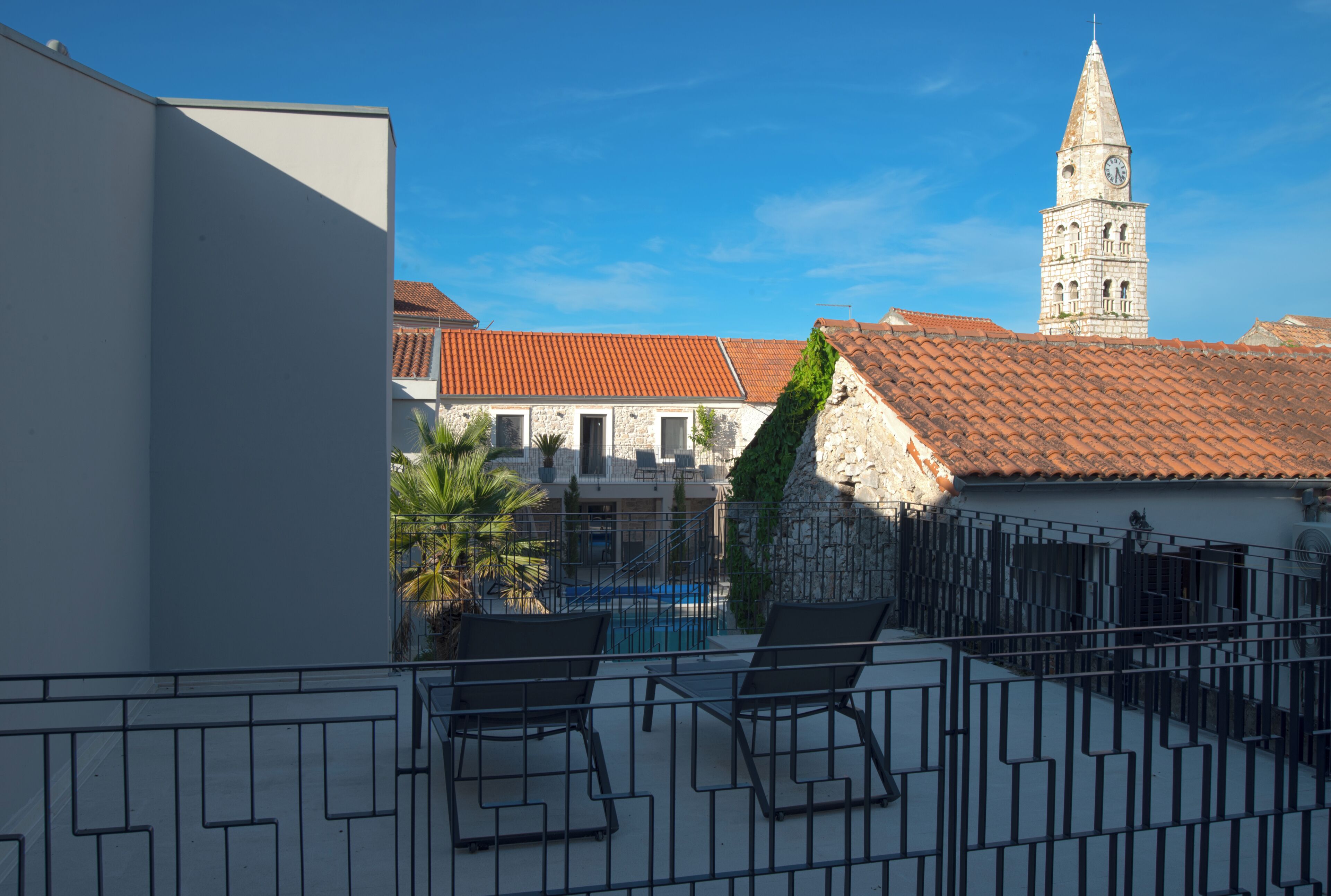 A rooftop terrace with a pool, lounge chairs, and a view of a historic building with a clock tower.
