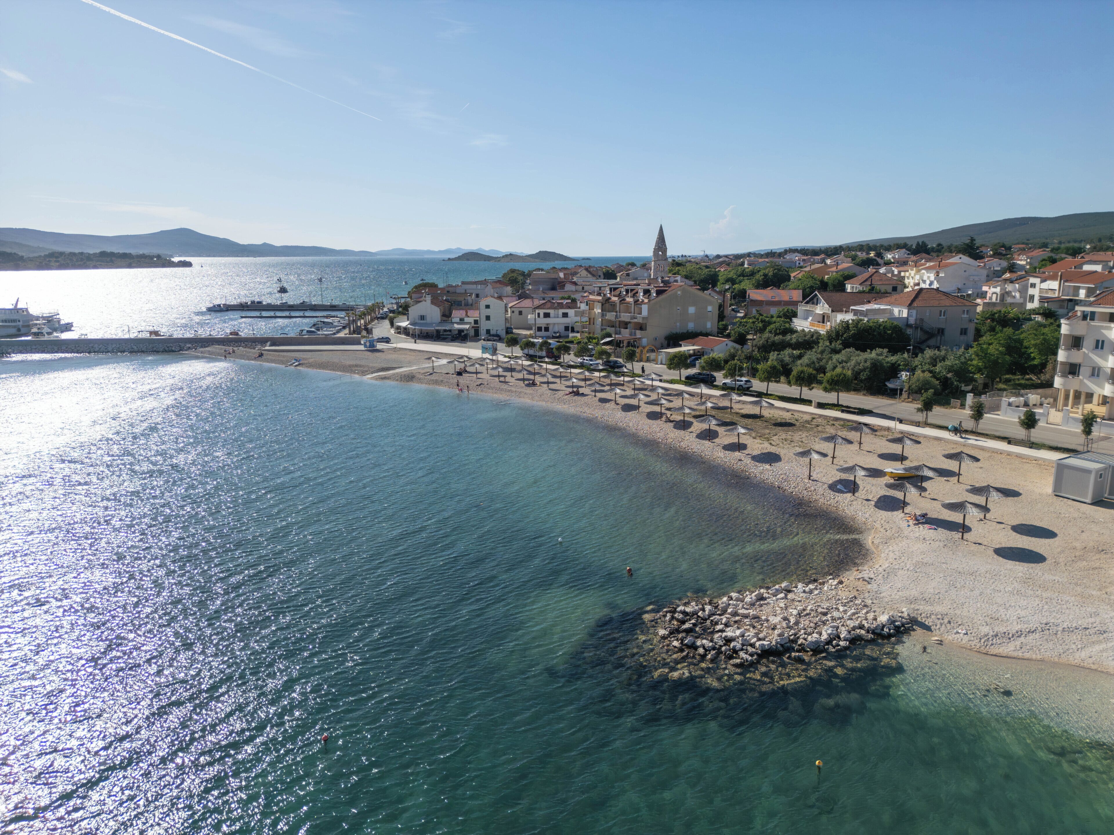 A coastal town with a beach, clear water, and buildings in the background.